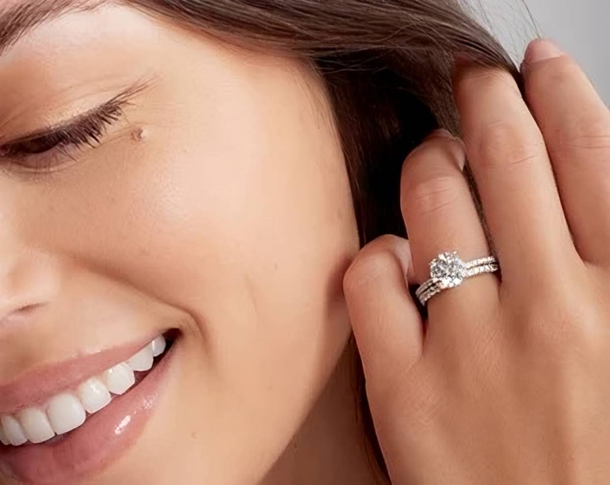 Jeune femme souriante portant une bague solitaire diamant accompagnée d’une alliance pavée en or blanc, symbole d’amour et d’élégance intemporelle.